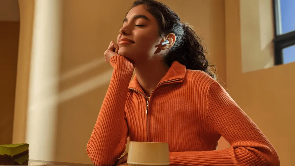 Kafedagi Redmi Buds 8 Active taqqan qiz — yarim quloqqa kiritiladigan quloqchin atrofdan ajratmaydi