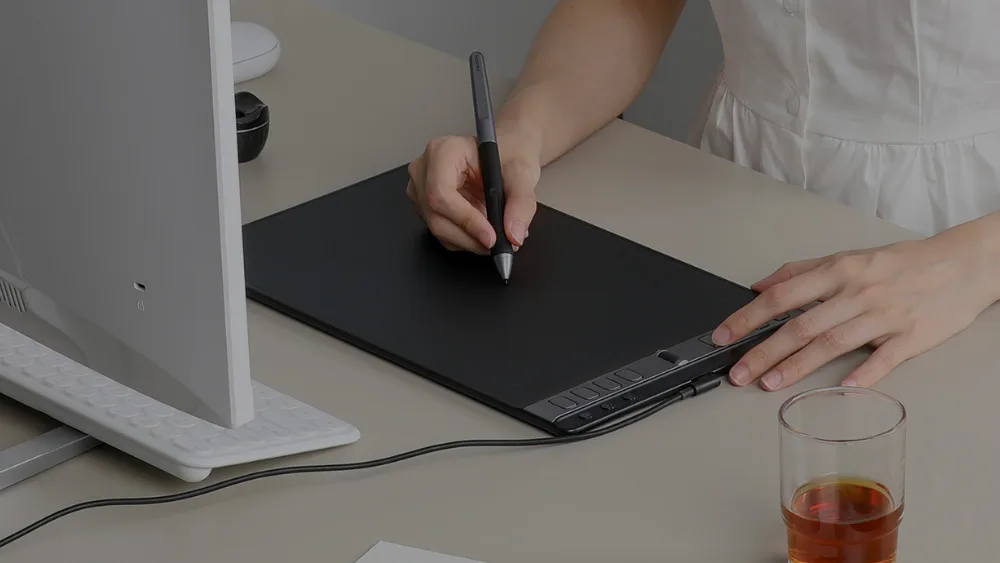 Stolda monitor oldidagi katta Huion Inspiroy 2 L, qoʻl pero bilan chizadi