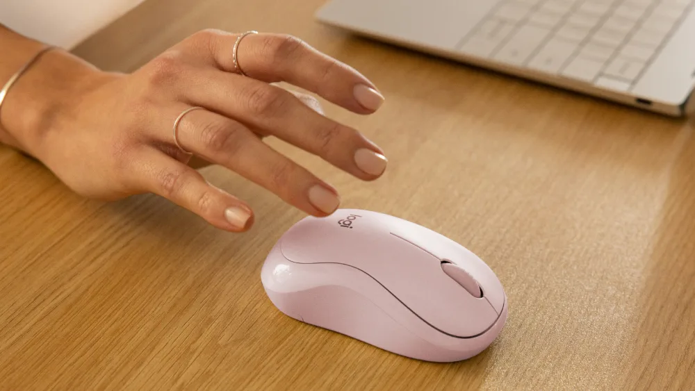 Noutbuk yonidagi pushti Logitech M240 Silent sichqonchasiga choʻzilgan qoʻl