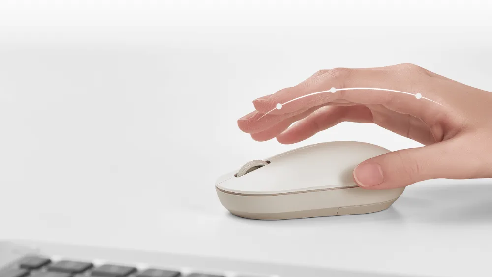 Oq stoldagi bej rangli yengil Xiaomi Wireless Mouse Lite 2 sichqonchasi ustida qoʻl