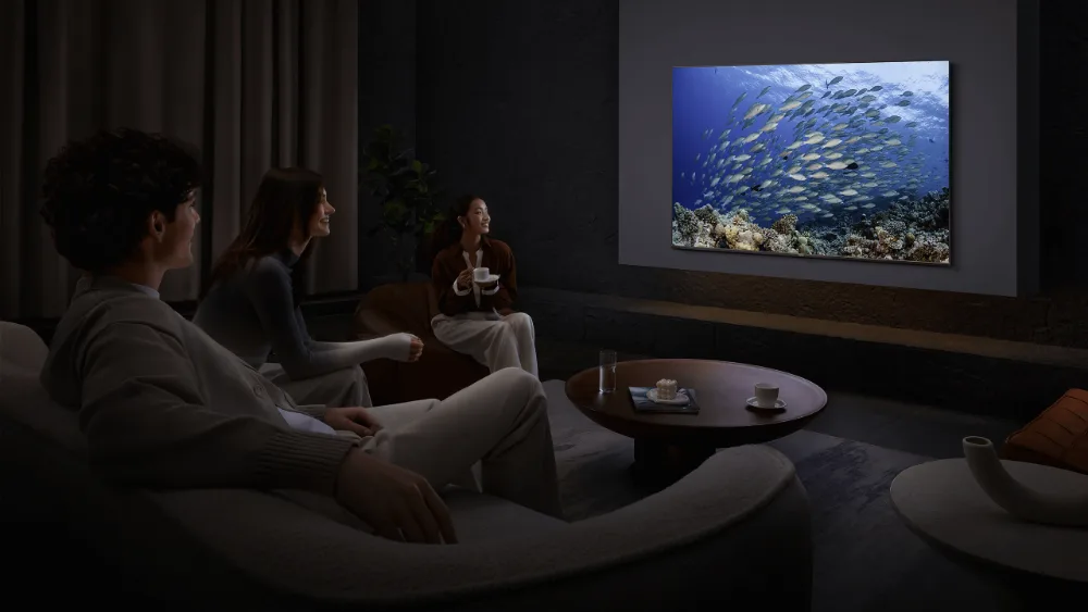 Qorongʻi mehmonxonada uch kishi Xiaomi TV A Pro 65 ni koʻrmoqda, ekranda baliqlar galasi