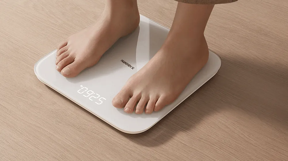 Yalangoyoq odam Xiaomi Smart Scale S200 tarozisida turibdi, displeyda ogʻirlik