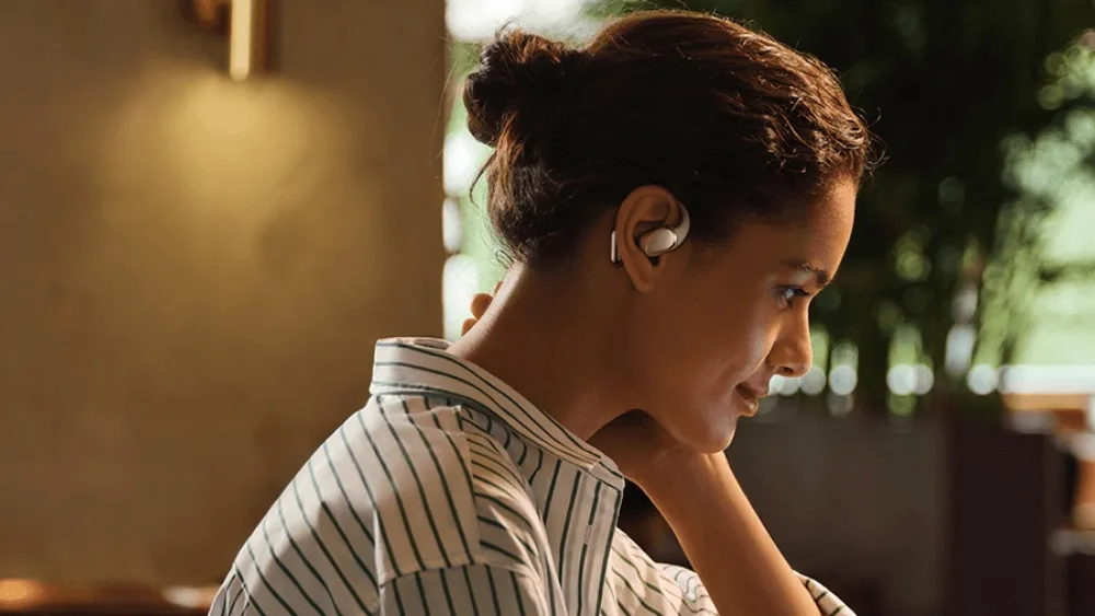 Noutbuk oldida Xiaomi OpenWear Stereo Pro taqqan qiz — quloqchin quloqqa ilingan va uni yopmaydi
